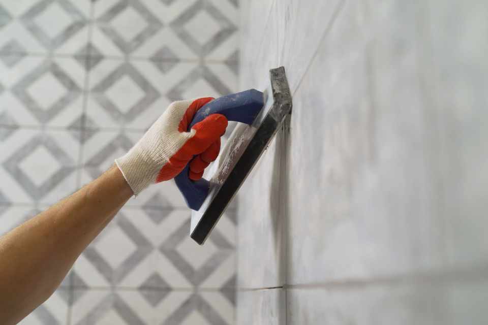 filling in grout with applicator on grey tiled walls